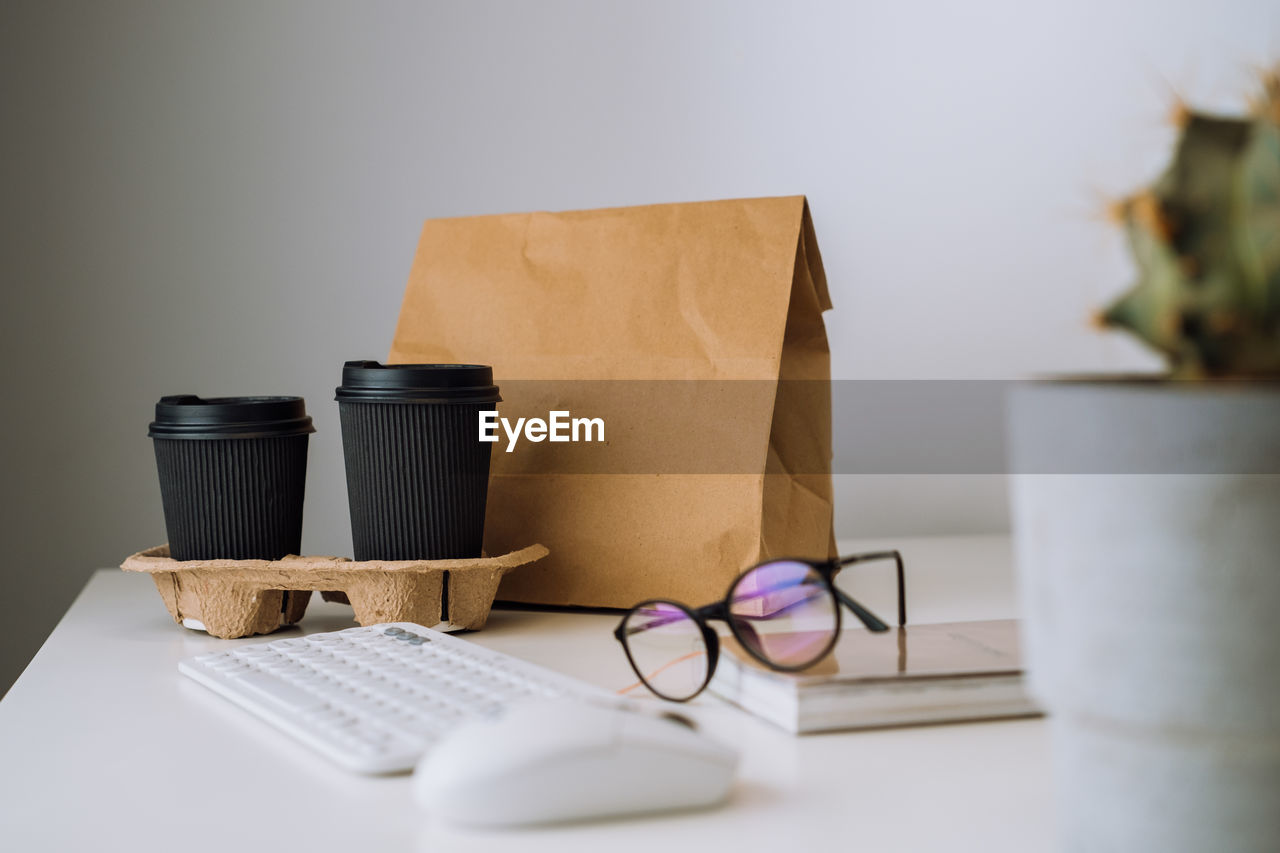 Package with food delivery and cups of coffee at workplace, glasses and notepad with keyboard