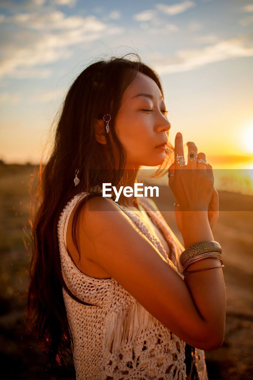 Beautiful asian girl in boho style standing at sunset on beach.