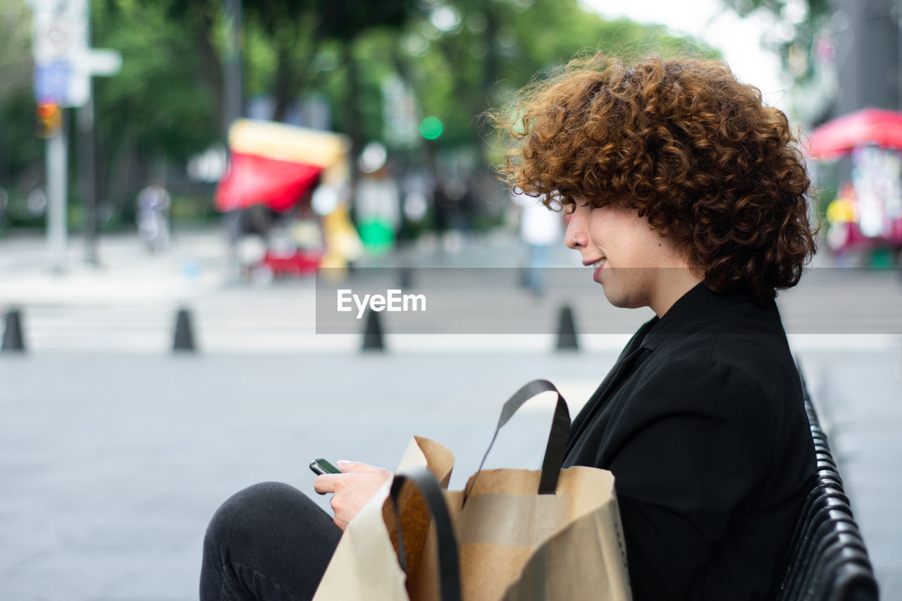 A happy non-binary person is sitting reviewing the smartphone