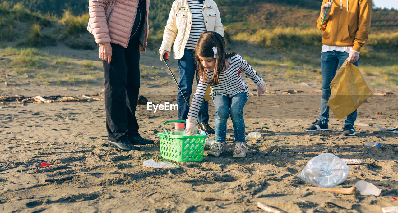 Girl putting plastic bottle into basket while standing at beach
