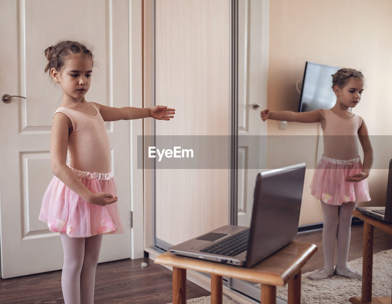 Pretty young ballerina practicing classic choreography during online class, social distance