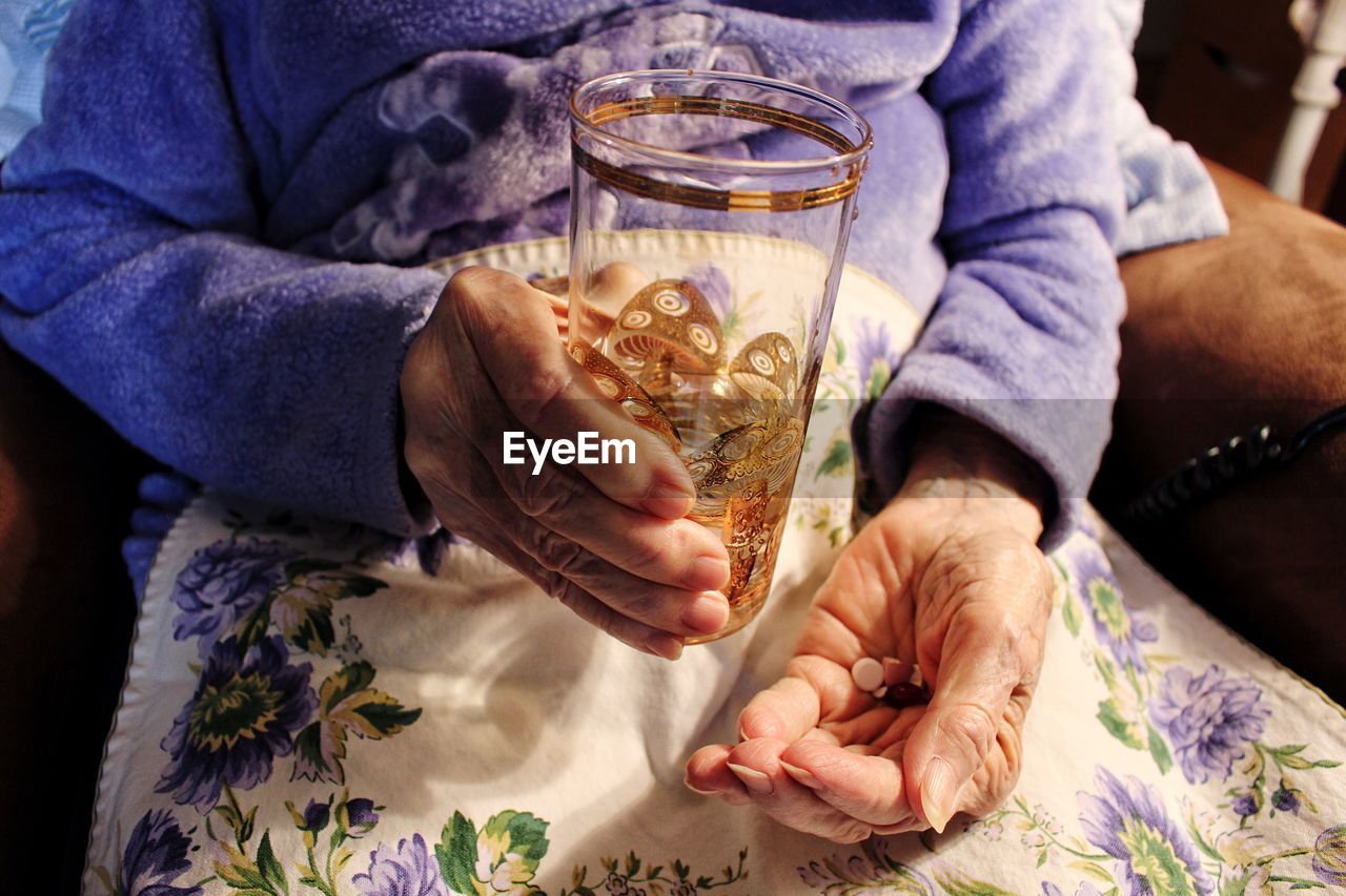 The elderly woman holds a glass in her hand and drinks medicine