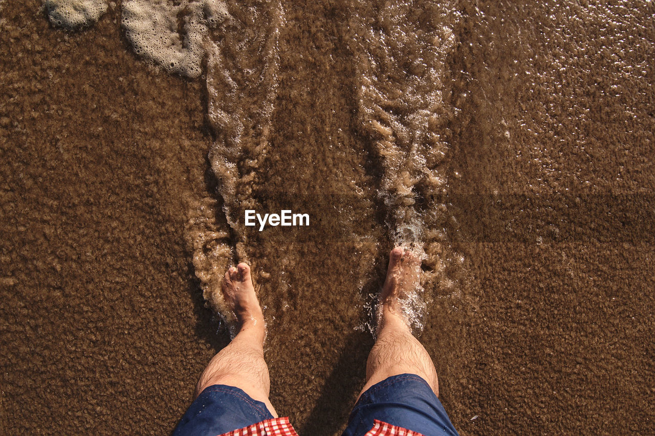 low section of man standing on sand