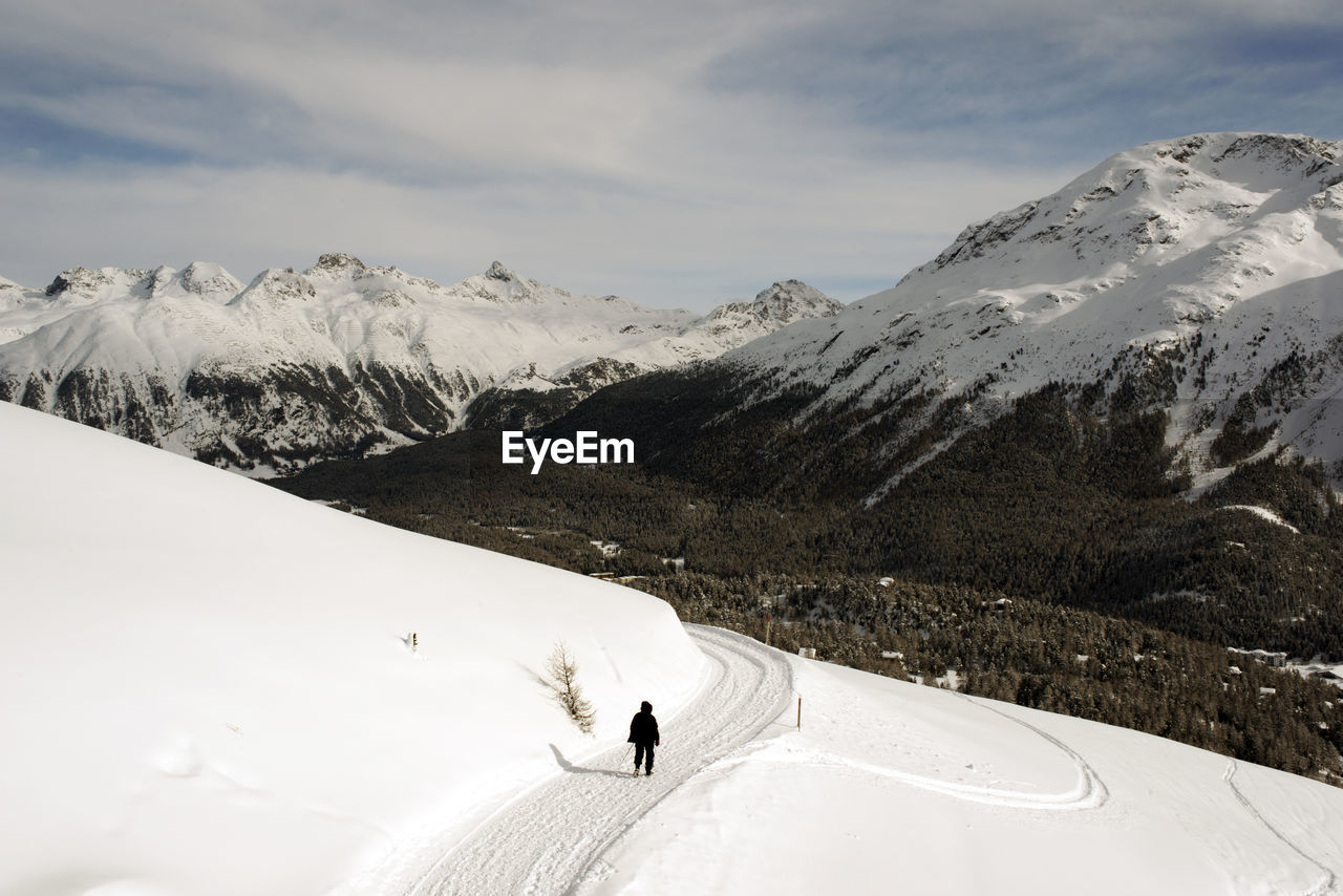 Rear view of person walking on snowcapped mountains against sky