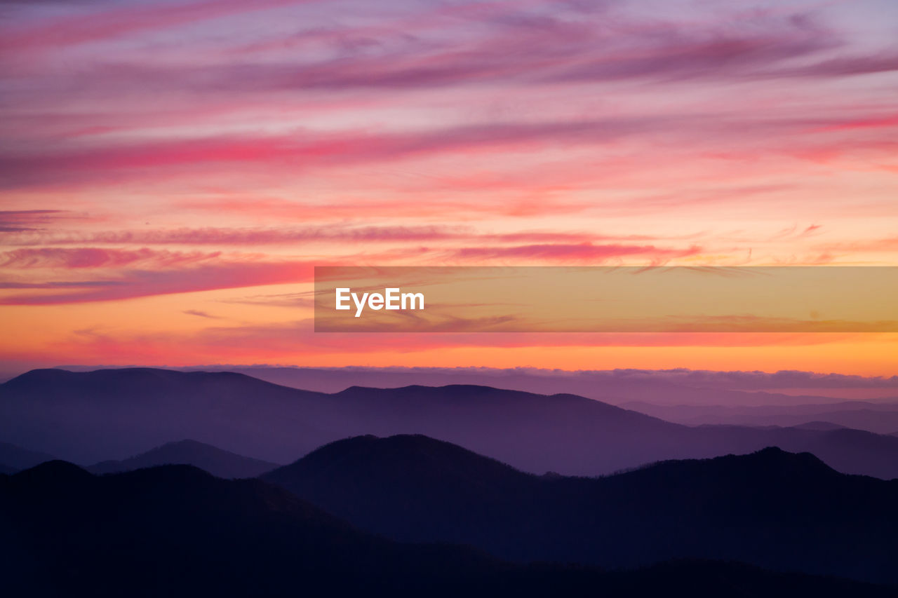 SCENIC VIEW OF SILHOUETTE MOUNTAINS AGAINST ORANGE SKY