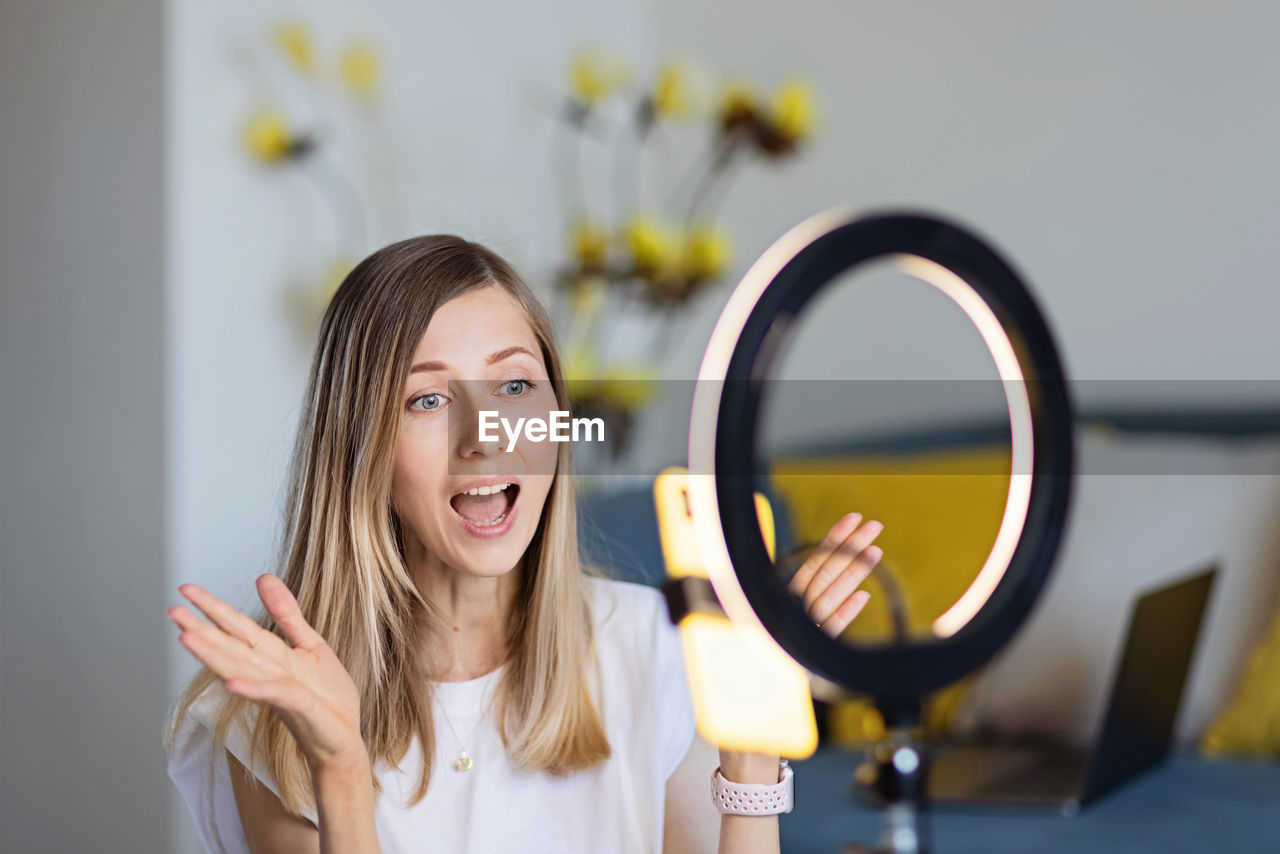 Young woman making photo or video content for social media with smartphone and light of ring lamp