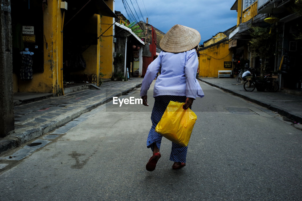 Rear view of person wearing asian style conical hat while walking on road