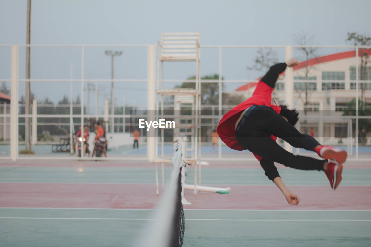 Young man jumping over net on court