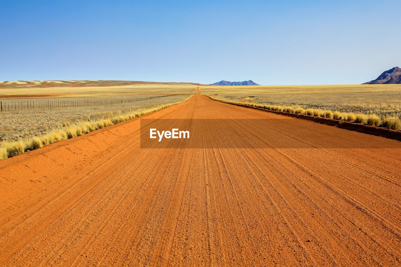 Tire tracks on agricultural field against clear blue sky