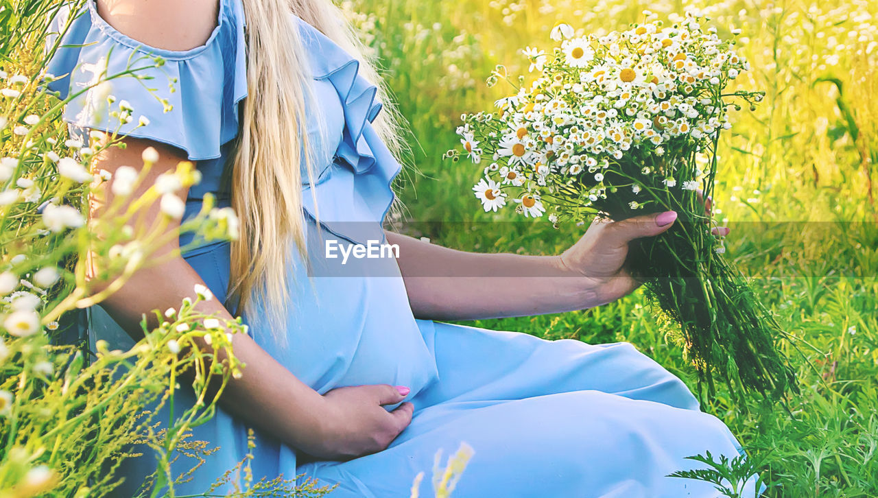 midsection of woman holding plant on field