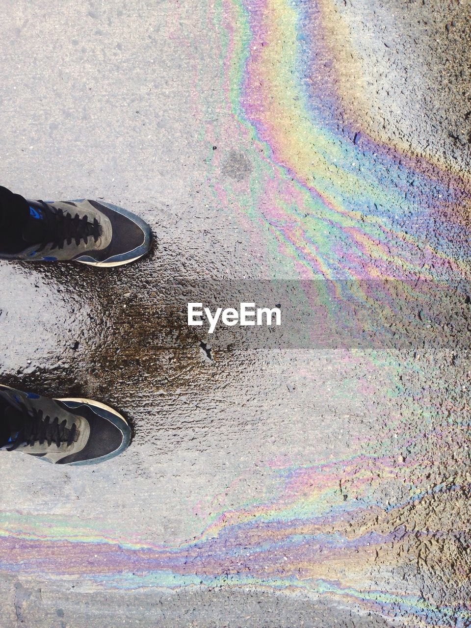 Low section of person standing on wet street with oil spill