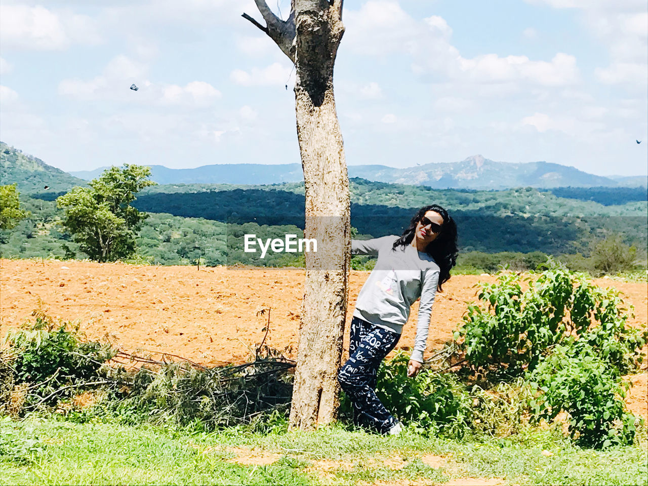 WOMAN STANDING ON FIELD BY TREE AGAINST SKY