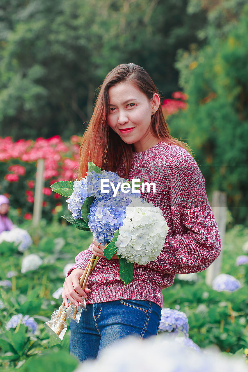 Mid adult woman standing amidst flowering plants at farm