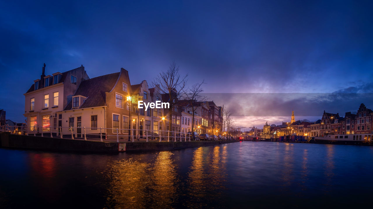 Illuminated buildings by river against sky at night