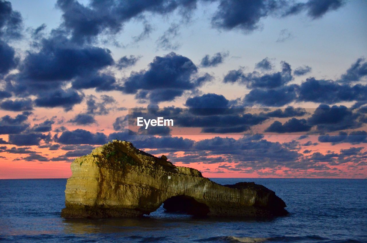 Rock formation in sea against sky during sunset