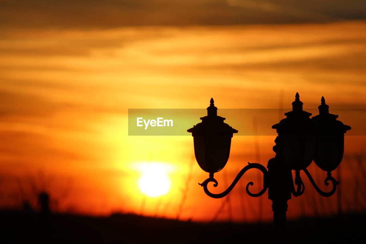 Silhouette lamp on field against orange sky