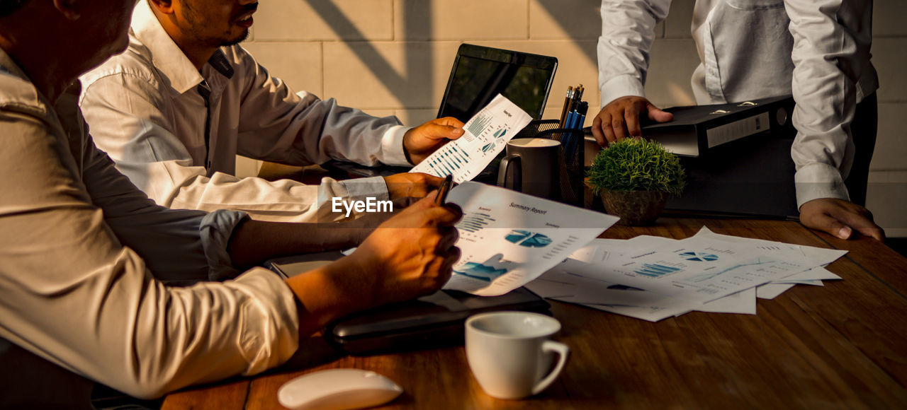 Midsection of colleagues working over graph in office