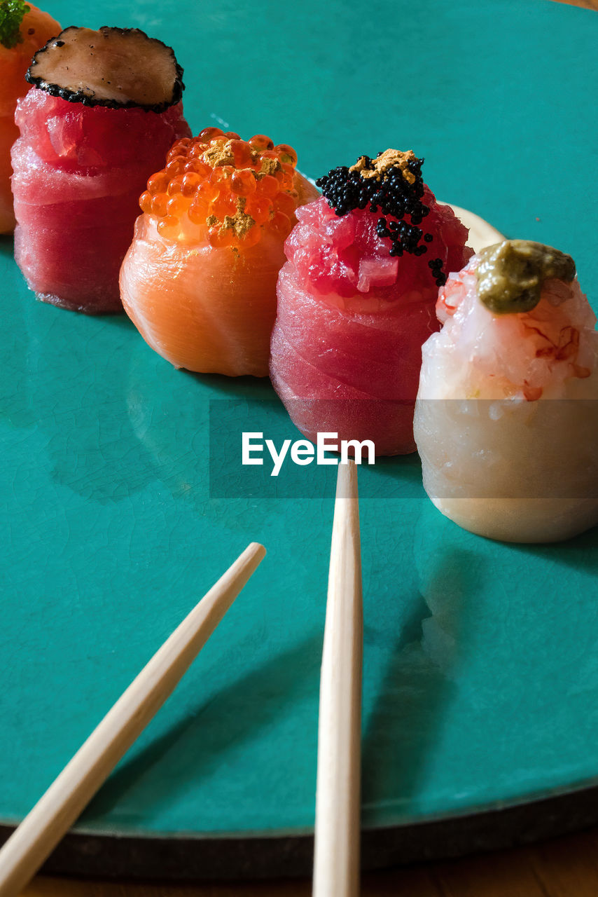 Assorted nigiri sushi, garnished with caviar and gold flakes, presented on a turquoise backdrop.