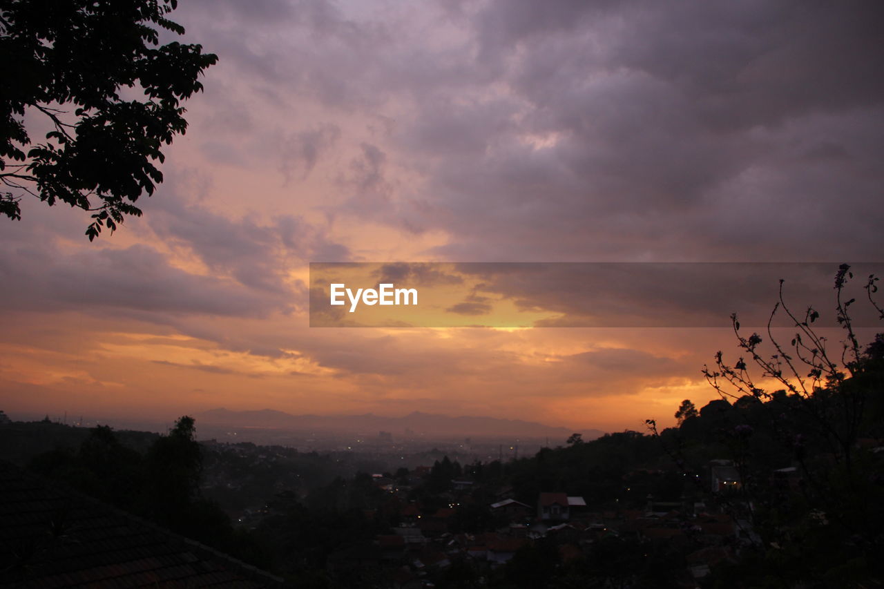 VIEW OF CITYSCAPE AGAINST CLOUDY SKY AT SUNSET