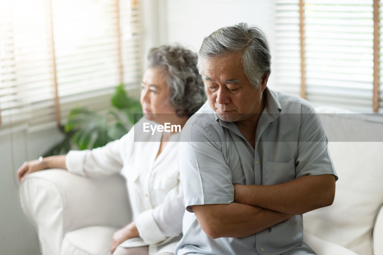 Unhappy senior couple sitting at home on sofa