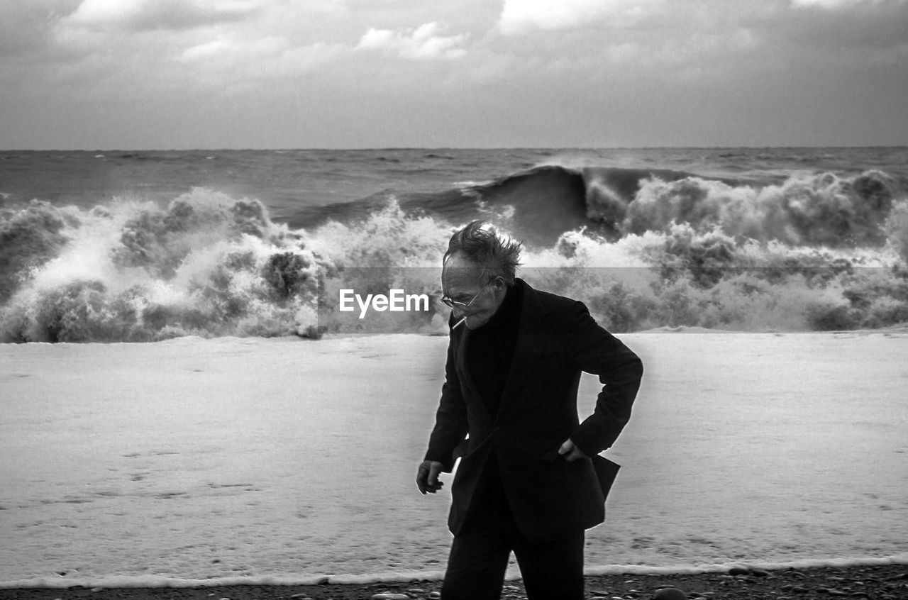 Senior man smoking cigarette while walking at seashore