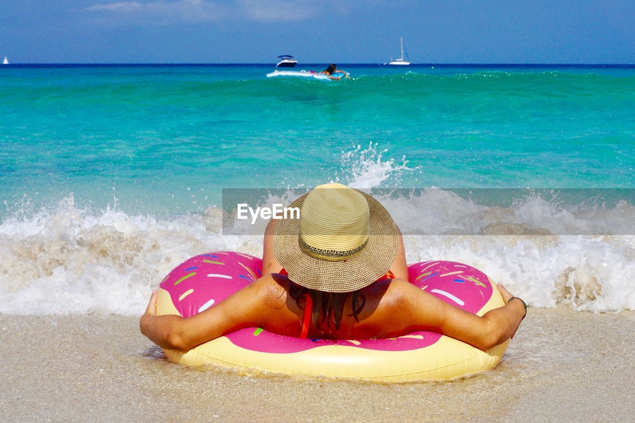 Rear view of young woman with inflatable ring relaxing at beach during sunny day