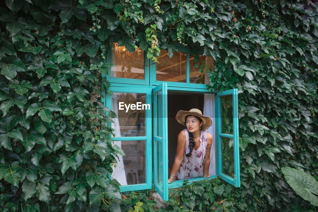 Woman standing against window of plants