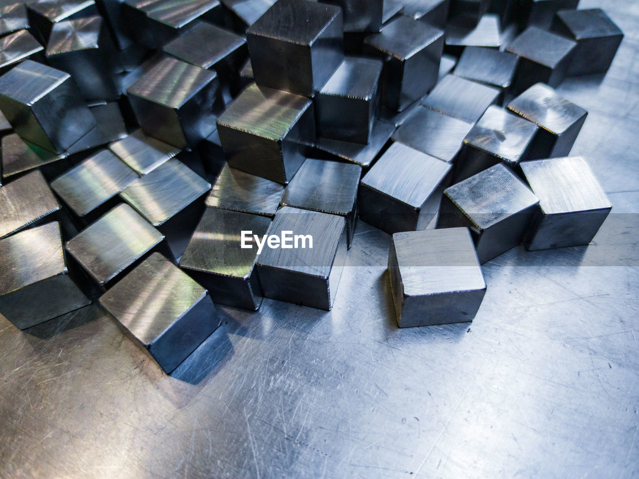 Pile of small machined shiny steel cubes on metal surface