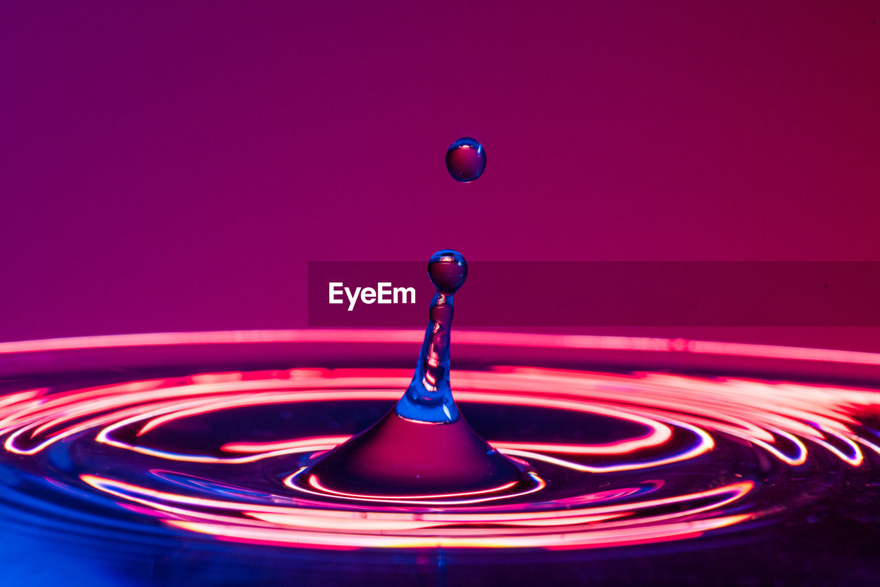 CLOSE-UP OF DROP FALLING ON BLUE WATER AGAINST PINK BACKGROUND