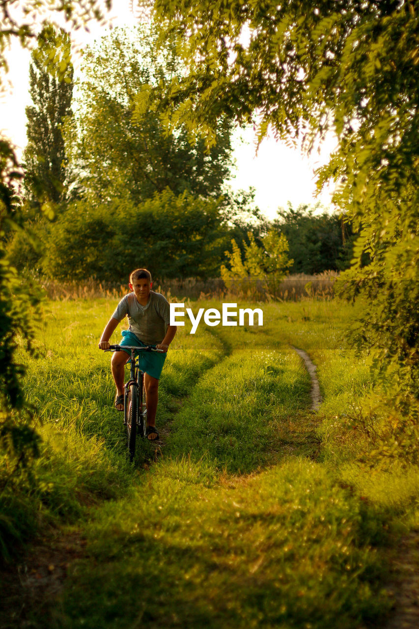 Happy childhood. a beautiful teenage boy rides a bicycle in the countryside path. nature green 