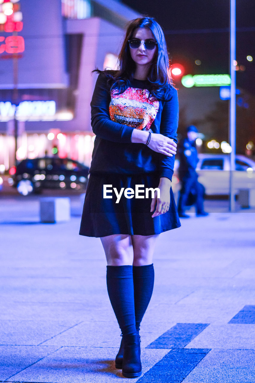 Full length portrait of fashionable young woman in city during night