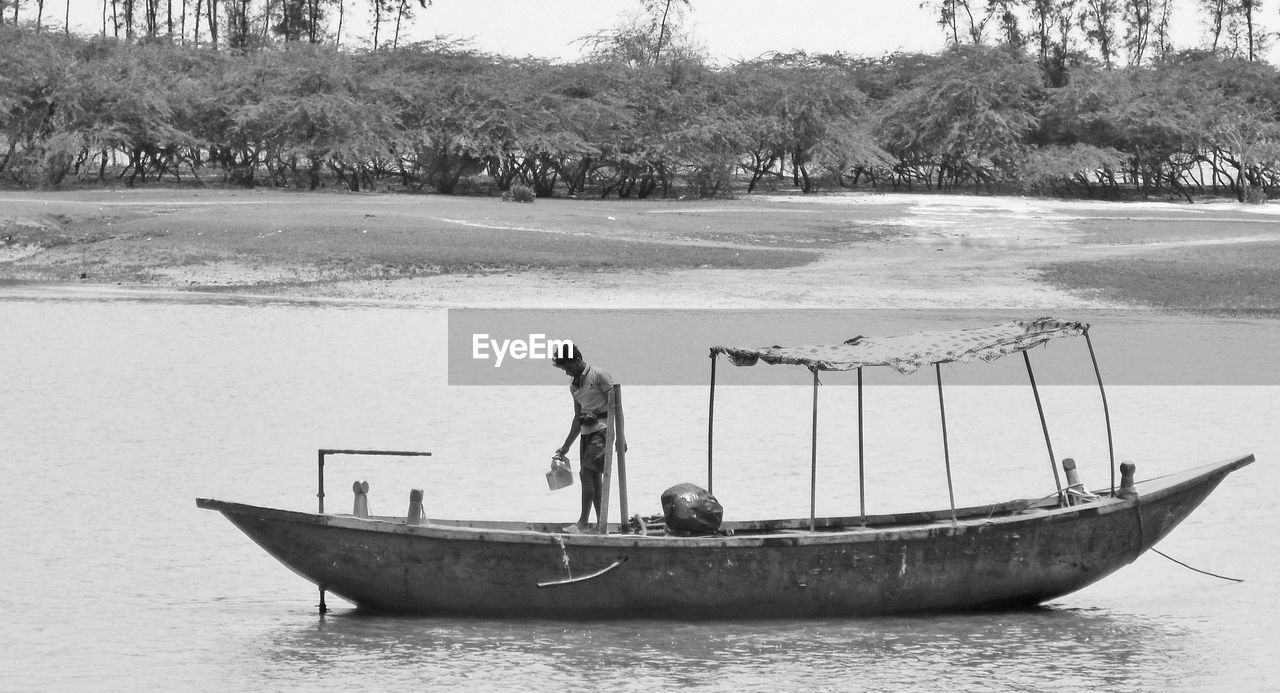 water, nautical vessel, transportation, mode of transportation, vehicle, boat, men, nature, tree, day, plant, sea, occupation, adult, watercraft, outdoors, travel, two people, land, beach, black and white, fisherman, lifestyles, sky, full length