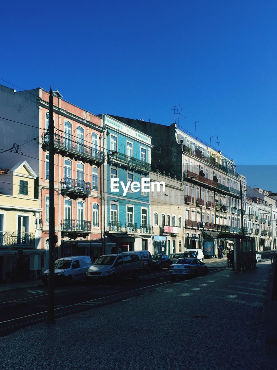 Cars on road by buildings against blue sky