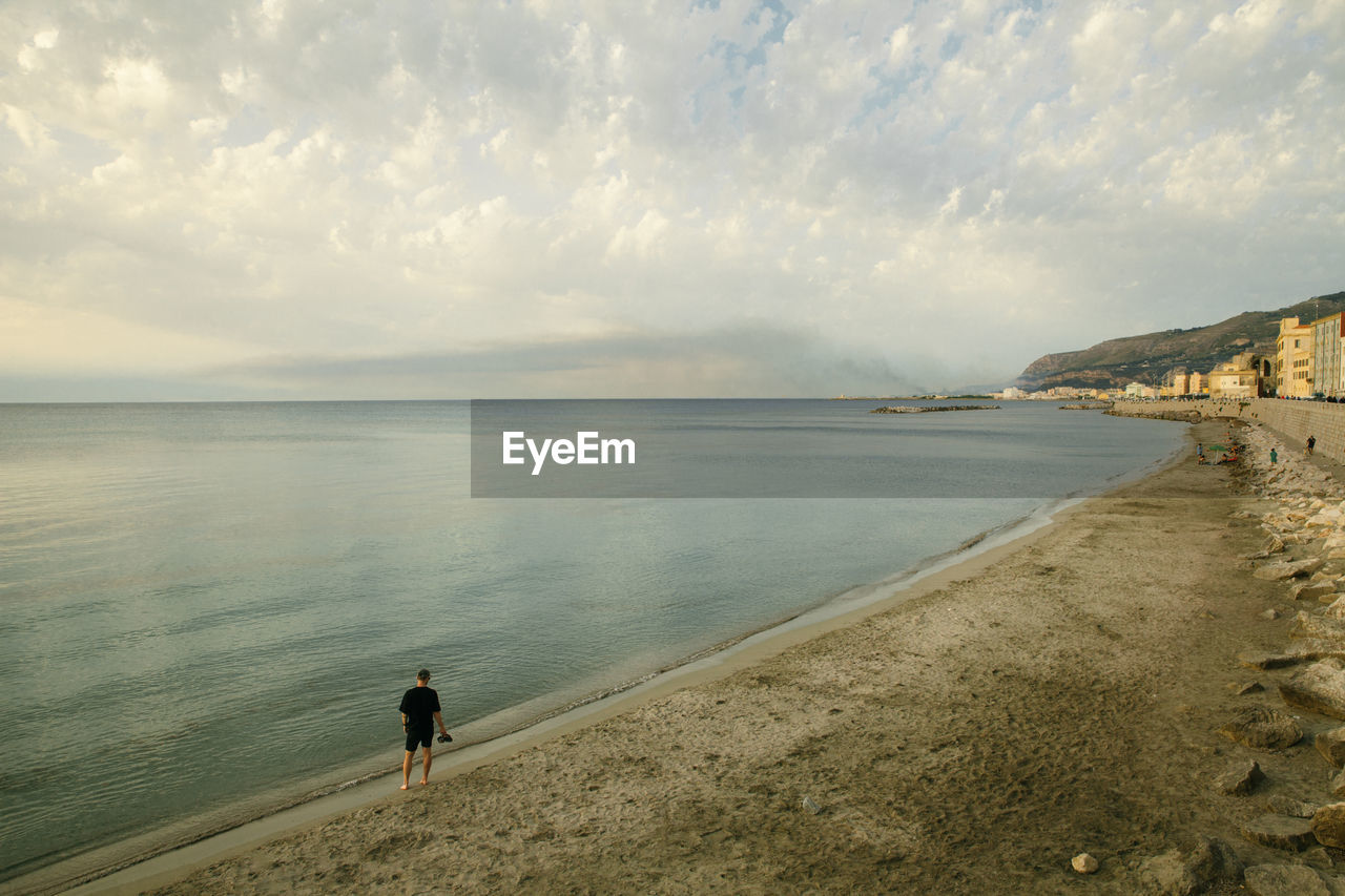 REAR VIEW OF MAN STANDING ON BEACH