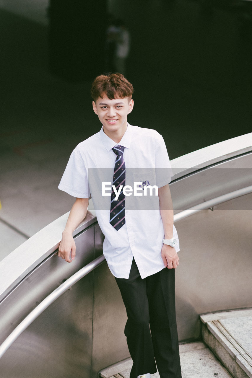 Portrait of young man standing against railing