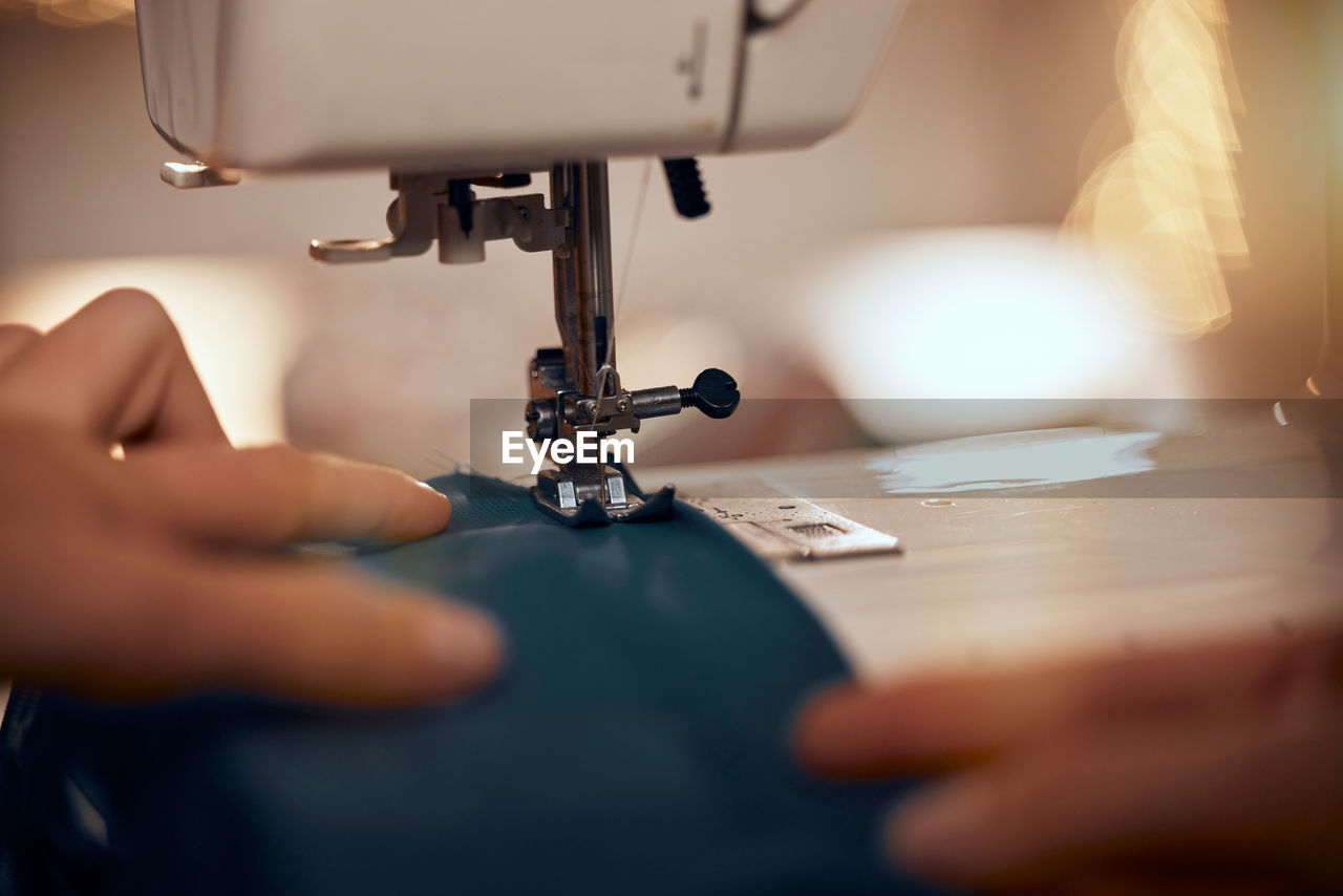 cropped hands of woman using sewing machine