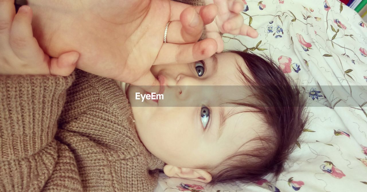 Close-up of baby sucking parent hand while tying on bed