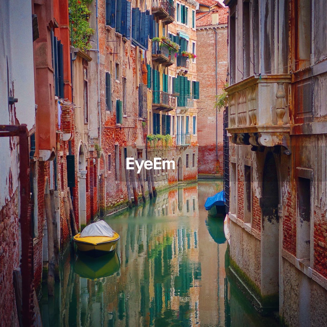 Covered boat in canal amidst buildings