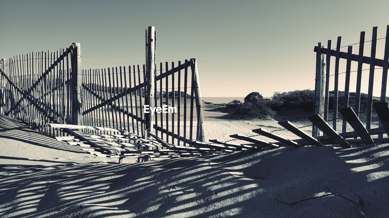 sky, nature, sunlight, shadow, no people, architecture, fence, land, winter, day, railing, line, outdoors, snow, black and white, scenics - nature, beach, clear sky, sunny, built structure, tranquility, landscape, sand, travel destinations, beauty in nature, tranquil scene, monochrome, security, water, environment, sea