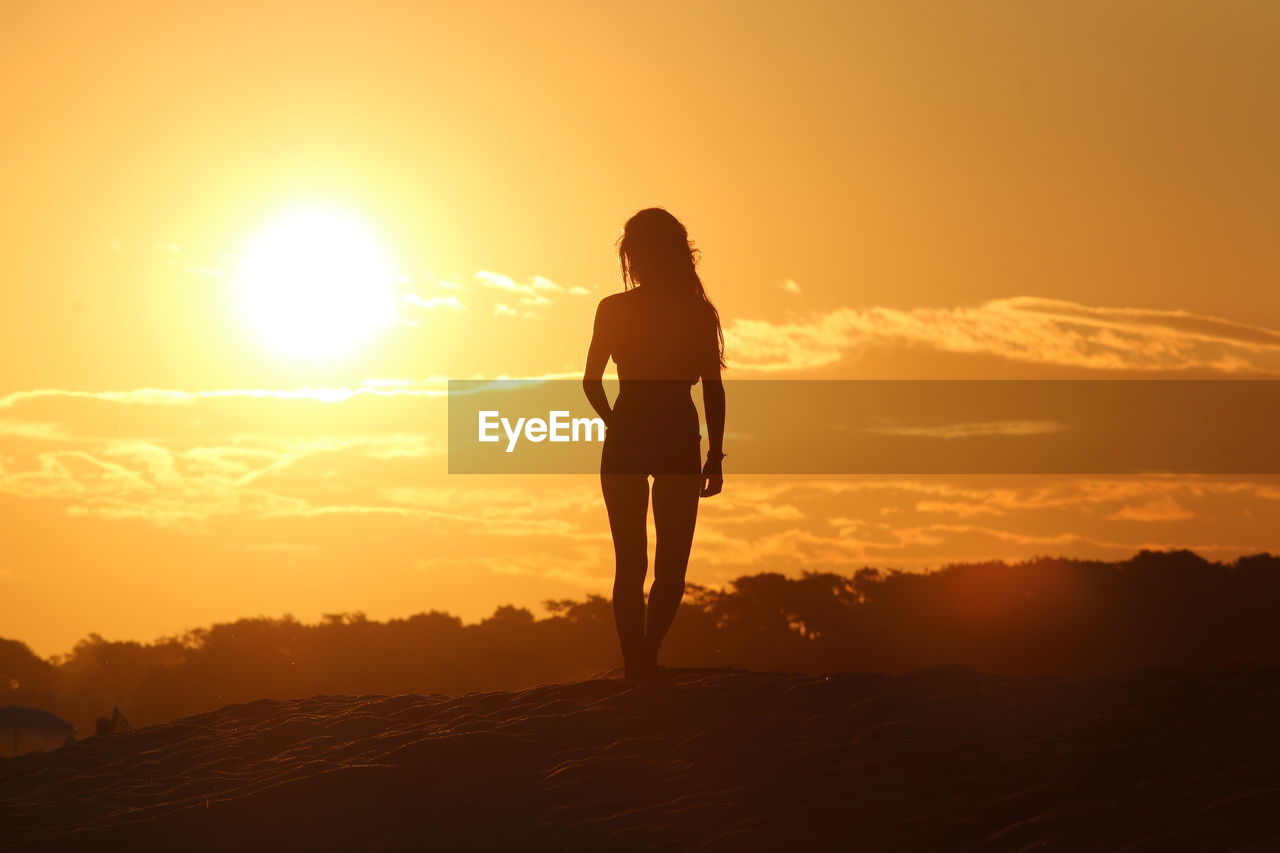 Silhouette woman standing on beach against sky during sunset