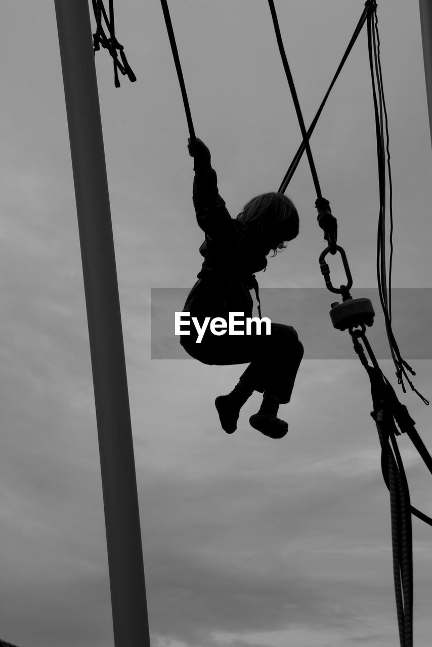 Low angle view of girl swinging against sky