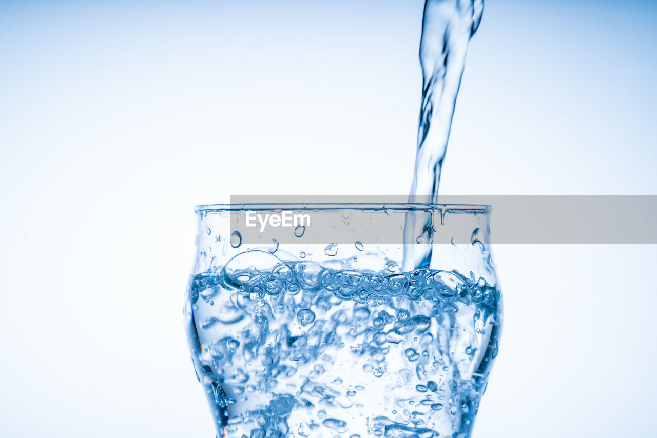 refreshment, water, drink, food and drink, blue, studio shot, splashing, drinking glass, glass, household equipment, soft drink, motion, freshness, indoors, drinking water, pouring, cold drink, transparent, cold temperature, drop, nature, no people, bubble, close-up, purity, cobalt blue, alcoholic beverage, white background, blue background, copy space