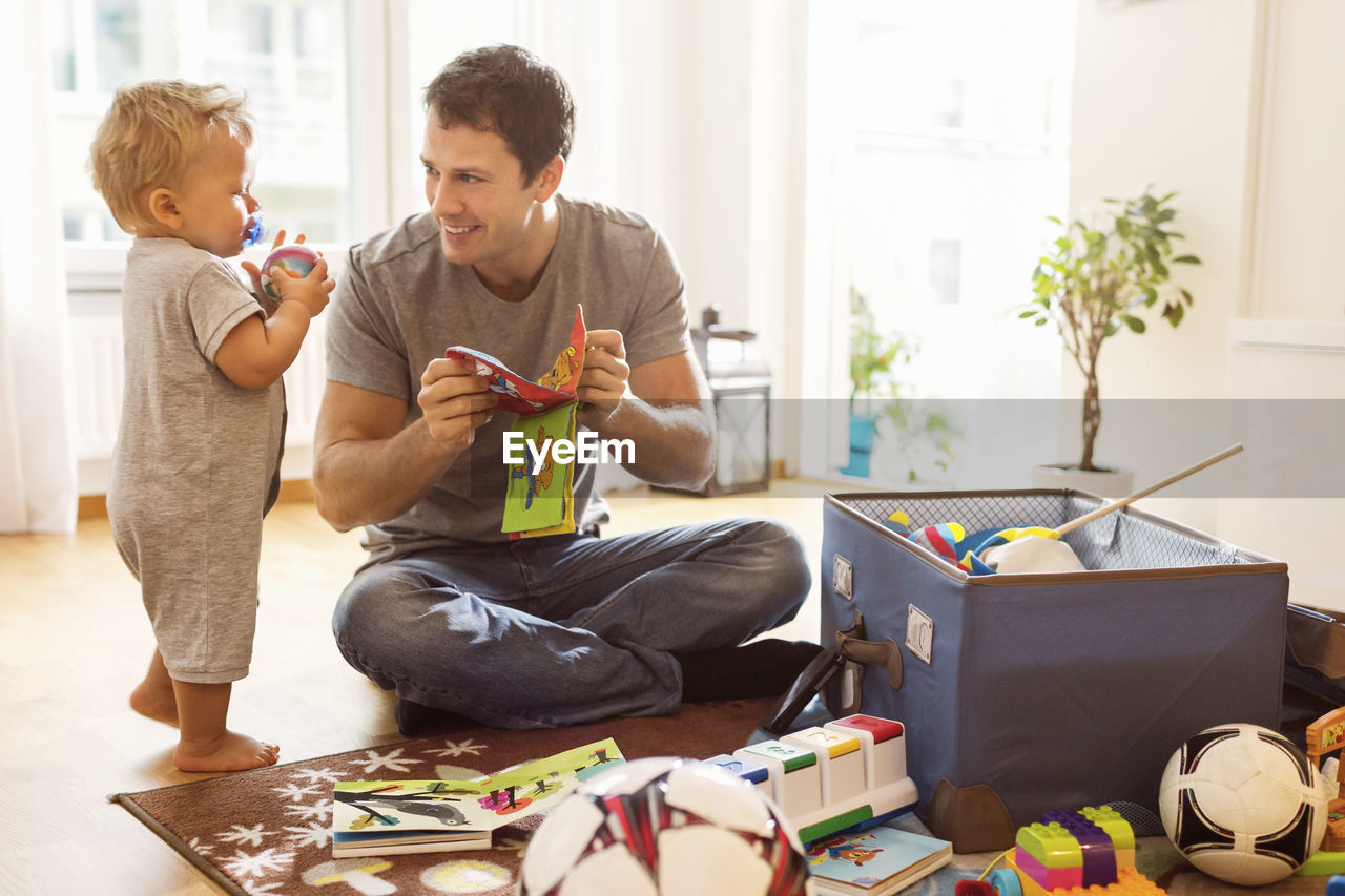 Smiling father showing toy to baby boy at home