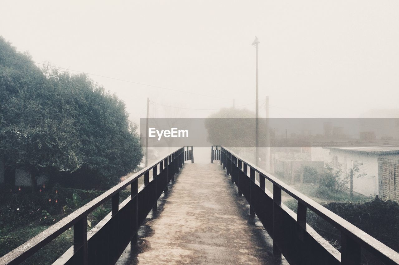 Empty footbridge against sky during foggy weather