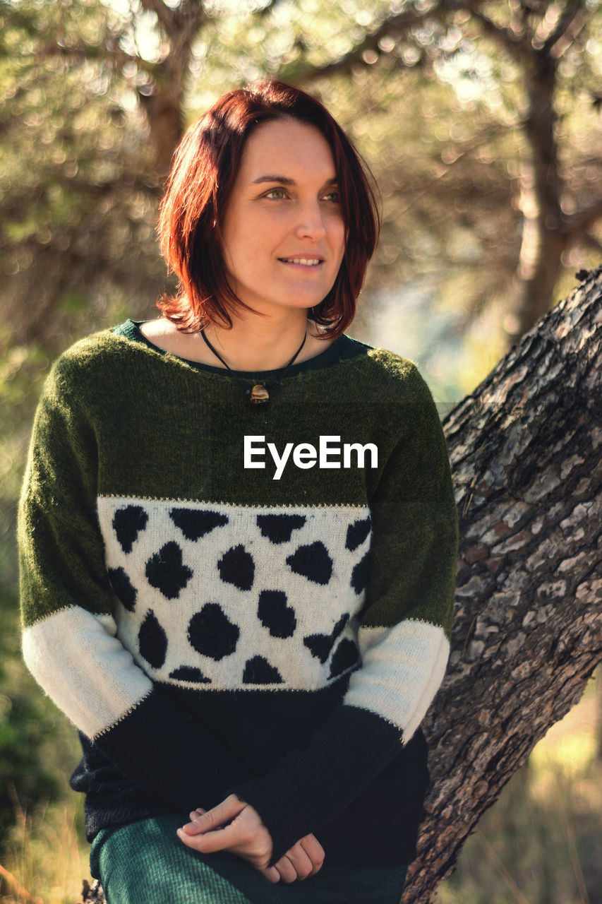 Model with red hair and sweater supported by a tree