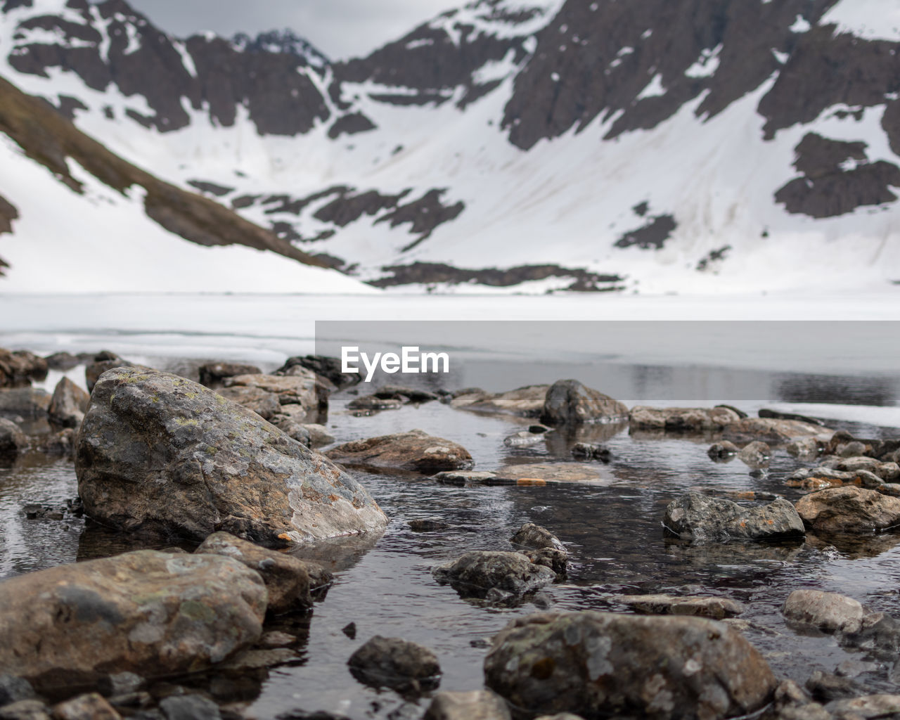 ROCKS IN SEA AGAINST SNOWCAPPED MOUNTAINS