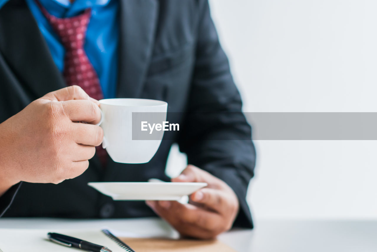 MIDSECTION OF MAN HOLDING COFFEE CUP AND LAPTOP