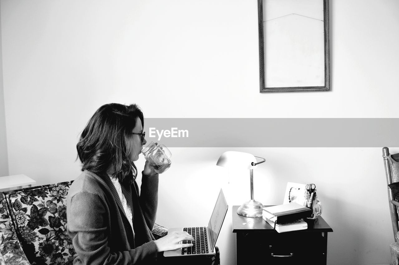 Woman drinking coffee while using laptop at home