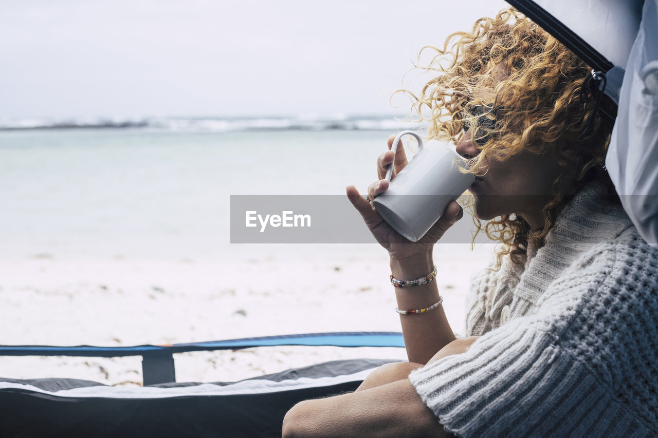 Woman drinking coffee while sitting at beach