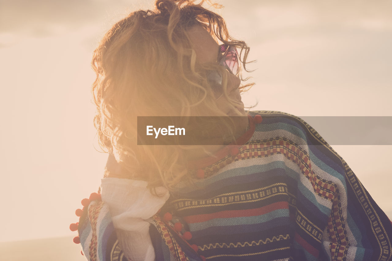 Close-up of woman with hand in hair against sky